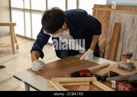 Asian man Carpenter working with technical drawing or blueprint construction paper lying on a workshop with carpentry tools and wood at home Stock Photo