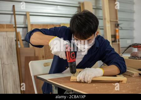Asian man Carpenter working with technical drawing or blueprint construction paper lying on a workshop with carpentry tools and wood at home Stock Photo