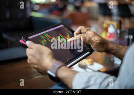 Asian business men using a tablet for working and checking stock trends chart and financial analysis at coffee shop Stock Photo