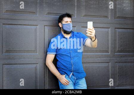 Smiling fashionable mature man taking selfie with protective face mask during covid-19 outbreak Stock Photo
