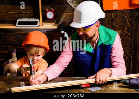 Dad shows his boy how to make diy in wooden workshop using hammer and nail. Father and son use carpenter toolsl. Little Builder. Stock Photo