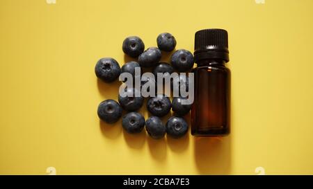 A bottle of blueberry seed essential oil and fresh blueberries on yellow background Stock Photo