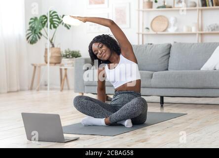 Sporty black girl exercising at home, using laptop