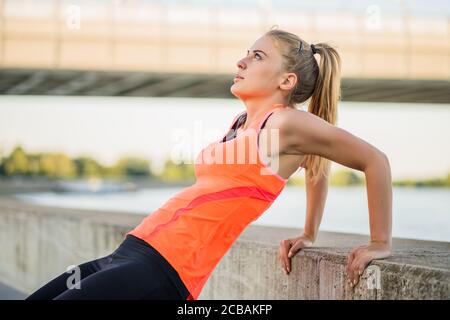 Young woman is exercising outdoor. She is doing reverse push-ups. Stock Photo