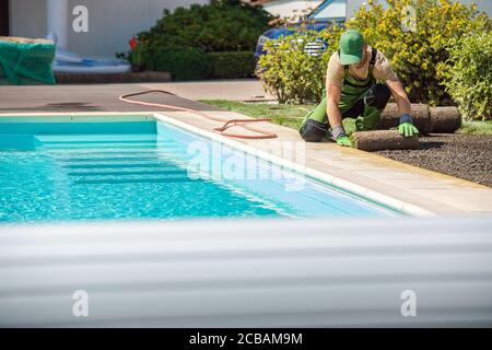 New Grass Turfs Installation Next to Residential Swimming Pool in the Backyard Garden. Caucasian Professional Landscaper at Work. Stock Photo