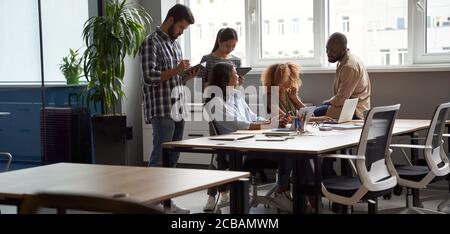 Successful project team in coworking space. Group of young multicultural business people working together in modern office, using laptop, tablet Stock Photo
