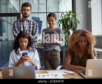 Group of young multicultural business people working together in modern office, using laptop, tablet, smartphone. Successful project team in coworking Stock Photo
