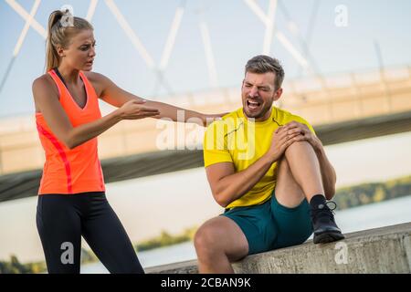 Young man is having pain in knee while exercising and jogging outdoor. Stock Photo
