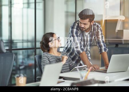 Having conversation at work. Young female and male colleagues talking and discussing project, working together in the modern coworking space Stock Photo