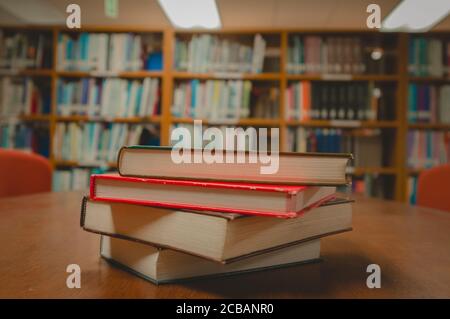 Stack of books on table and blurred bookshelf in the library room, education background. Stock Photo