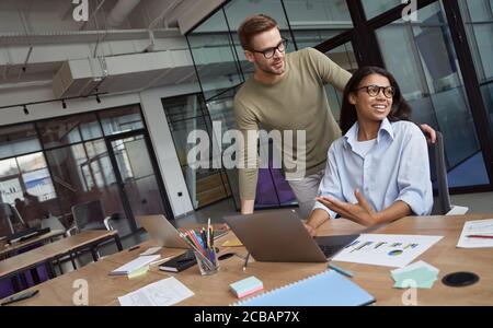 Teaching new employee. Group of two happy colleagues working together in the modern coworking space, talking and communicating Stock Photo