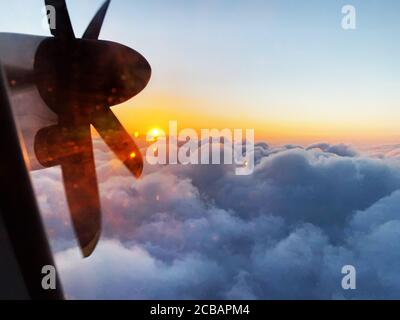 Romantic view from the window of a propeller flight into the rising sun during a flight above the clouds. Stock Photo