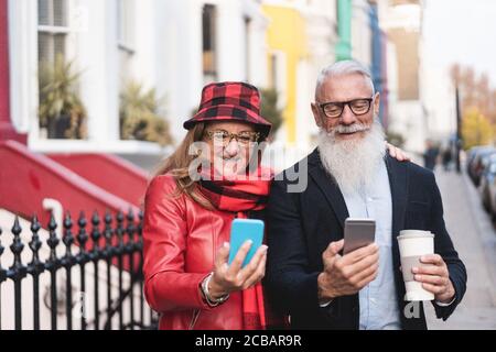 Senior fashion couple using smartphone app during fall vacation - Mature people having fun with technology trends - Travel, tech, love and joyful elde Stock Photo