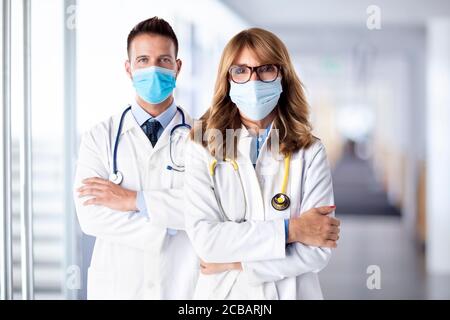 Shot of female and male doctors standing together on the clinic’s foyer while looking at camera. Medical team. Doctors wearing face masks for preventi Stock Photo