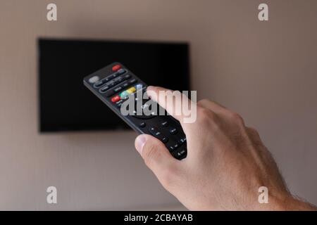 Male hand with tv remote control and blurred television with a black screen in the background. Man changes channels on the TV Stock Photo