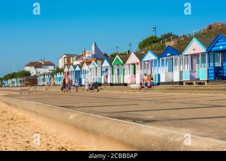 Suffolk seaside, view in summer of people sitting outside their colourful beach huts along the seafront in Southwold on the Suffolk coast, England, UK Stock Photo