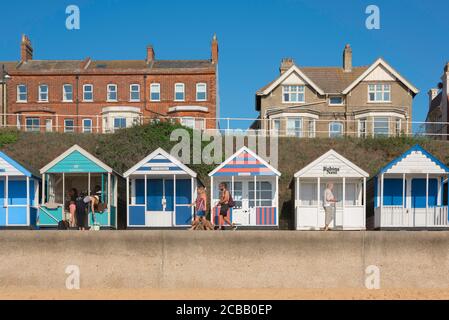 Suffolk seaside, view in summer of people walking past colourful beach huts along the seafront in Southwold on the Suffolk coast, England, UK