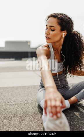 Fitness woman sitting outdoors and stretching. Sporty woman doing some stretching exercises in morning. Stock Photo