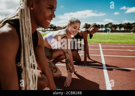 Three female athletes at starting position ready to start a race. Sprinters ready for race on racetrack. Stock Photo