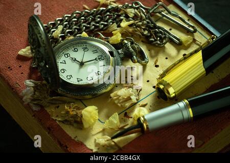 Vintage pocket watch and brass pen on old book. At 8 o'clock in morning. Education and vintage style concept. Stock Photo