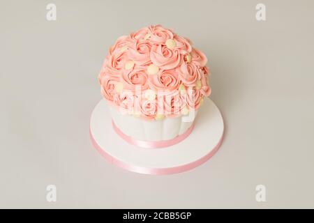 Homemade victoria sandwich giant cupcake with pink buttercream swirls and white chocolate buttons on top to decorate with jam filling and pink ribbon Stock Photo