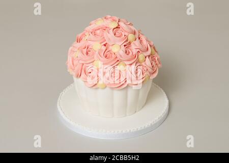 Homemade victoria sandwich giant cupcake with pink buttercream swirls and white chocolate buttons on top to decorate with jam filling and pink ribbon Stock Photo