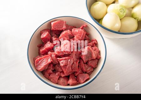 Cooking stew or goulash with diced beef and al lot of peeled onions, these two ingredients in bowls from above on a white table, selected focus Stock Photo
