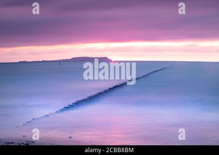 Long exposure of clouds above smooth ocean  within sunset. Line of a wooden breakwater. Stock Photo