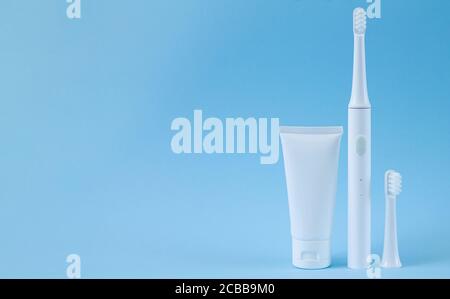 Smart electric toothbrush with spare head and toothpaste on blue background. Professional oral care concept Stock Photo
