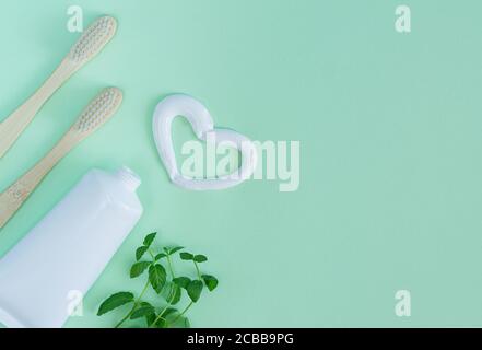 Bamboo toothbrushes, white tube of toothpaste, mint leaves on light green background. Heart shape created from tooth paste. Top view, copy space Stock Photo