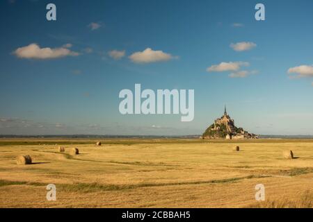 Beautiful view of famous historic Le Mont Saint-Michel tidal island in beautiful golden evening light at sunset in summer with hay bales on empty fiel Stock Photo