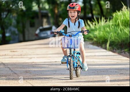 Happy girl riding a bike in garden park . Active child wearing bike helmet. Safety sports leisure with kids concept Stock Photo