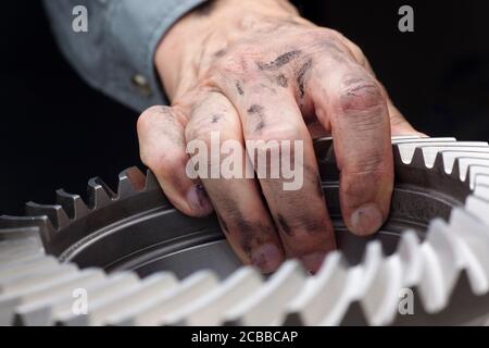 Close-up of a dirty hand of a repairman with a cog wheel in his hand - selective focus Stock Photo