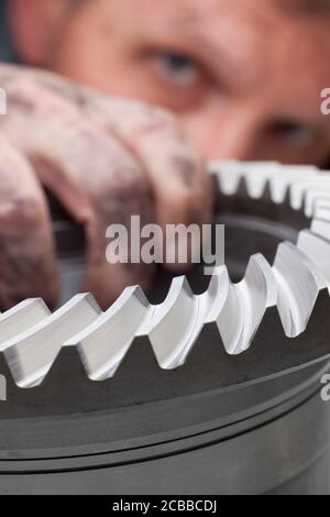 Mechanic examining a spare part - cog wheel - focus on the cog Stock Photo