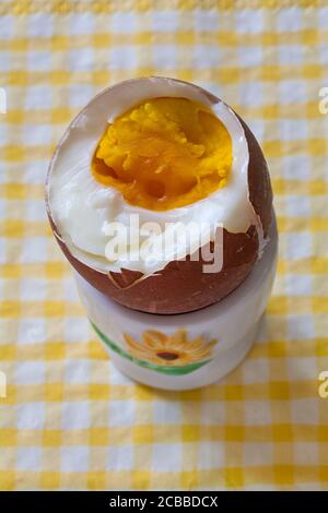 M&S British Farmed Free Range Maran Island Brown Egg in egg cup on yellow & white checked napkin serviette - boiled egg with top cut off  to show yolk Stock Photo
