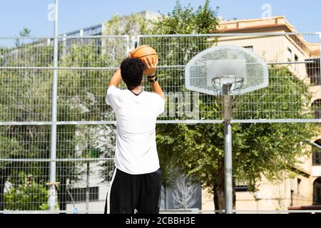 Afro teenage boy throwing a ball into a basket on the basketball court Stock Photo