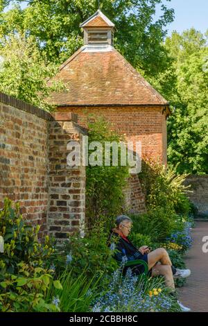 A man sits on a bench at Eastcote House Walled Garden with the Grade II listed 18th century Dovecote in the background. Hillingdon, London Stock Photo