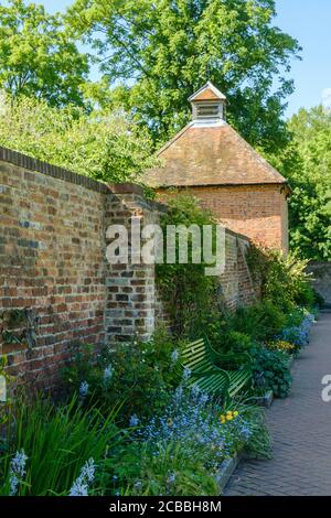 Empty park bench with flowers and old brick wall. Grade II listed 18th century Dovecote in the background. Eastcote Walled Garden, Hillingdon, London Stock Photo