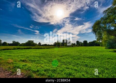 Blue sky, sun and veil clouds over a meadow Stock Photo