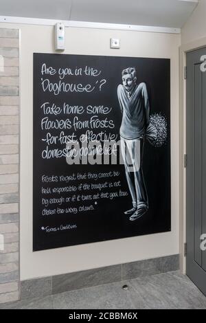 Quirky sign in a gents loo suggesting a man in the doghouse should buy his partner flowers; Frosts Garden Centre, Woburn, UK Stock Photo