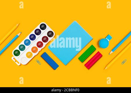 Back to school flat lay with blue and yellow pencils,watercolor, plasticine, whistle and notepads on yellow background. Stock Photo