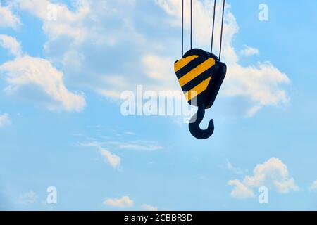 Heavy duty hooks on ropes with yellow-black guides in front of a white-blue sky with clouds Stock Photo