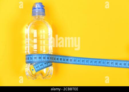 Bottle of water and fitness equipment on yellow background. Sports tools in cyan blue. Shaping and refreshment concept. Centimeter wrapped around bottle, top view. Stock Photo
