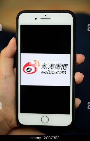 A hand holding a iPhone with logo of Sina Weibo/Weibo a Chinese microblogging social media platform on the screen Stock Photo