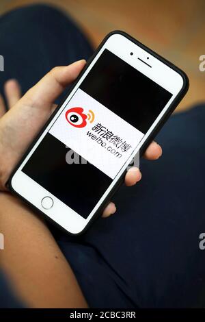 A hand holding a iPhone with logo of Sina Weibo/Weibo a Chinese microblogging social media platform on the screen Stock Photo