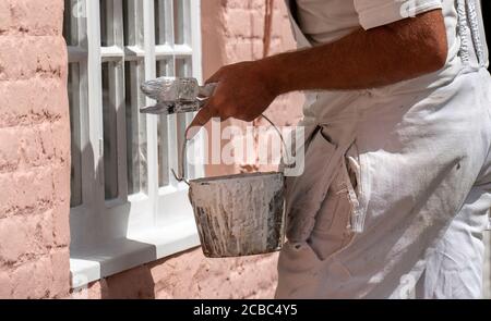Hampshire, England, UK. 2020. Painter decorator painting small windows on a rural house. Painters kettle and brushes.