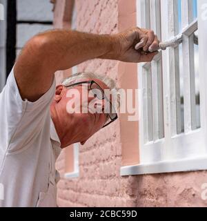 Hampshire, England, UK. 2020. Painter decorator painting small windows on a rural house