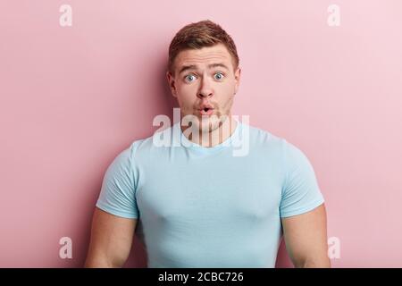 surprised emotional bug-eyed young man wearing casual blue t-shirt staring at camera with shocked look, expressing astonishment and shock, isolated pi Stock Photo
