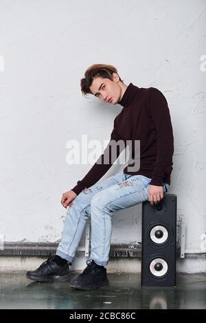 young handsone dancer having a rest, sitting on a musical column in the studio.full length photo, lifestyle, free time, spaare time Stock Photo