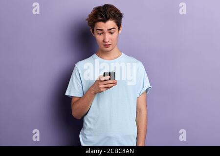puzzled scred man holding mobile phone, being shocked that he was stolen by fraudsters, crime concept. emtion and feeling Stock Photo